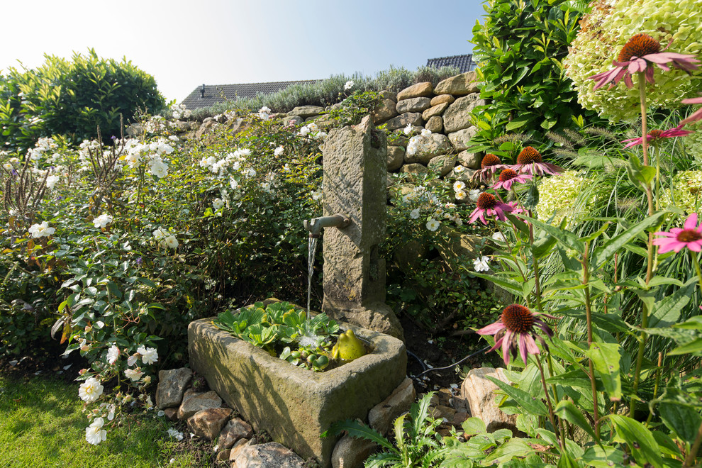 Exempel på en klassisk trädgård i delvis sol på sommaren, med en fontän och naturstensplattor