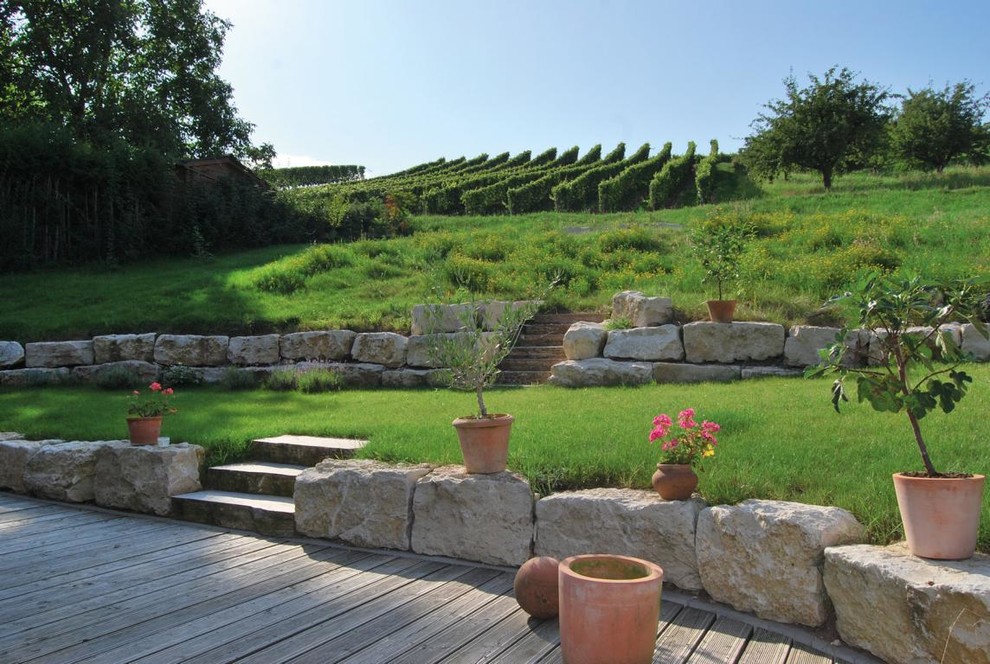 Ejemplo de jardín campestre grande en verano en ladera con muro de contención, adoquines de piedra natural y exposición parcial al sol