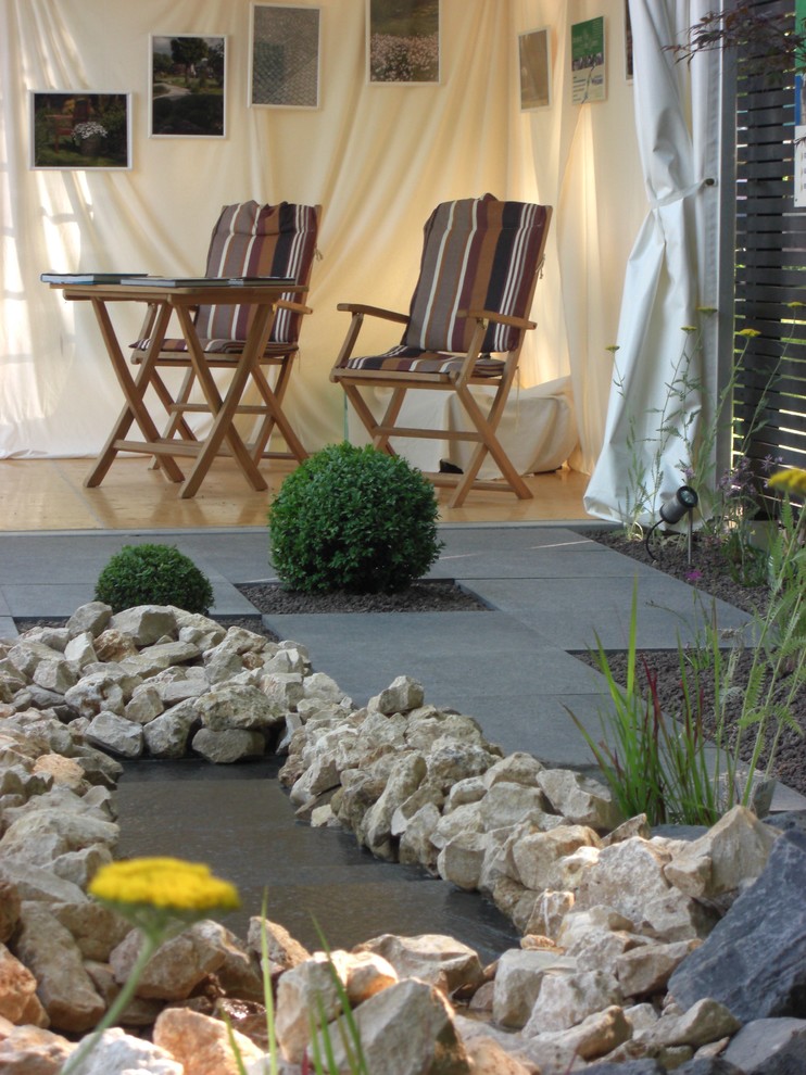 Inspiration för en liten funkis formell trädgård i delvis sol längs med huset på sommaren, med en fontän och naturstensplattor
