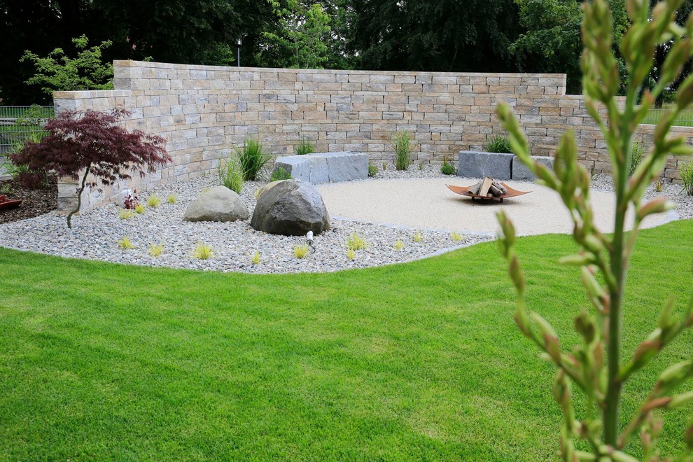 Foto di un grande giardino esposto in pieno sole dietro casa con un muro di contenimento e pavimentazioni in pietra naturale