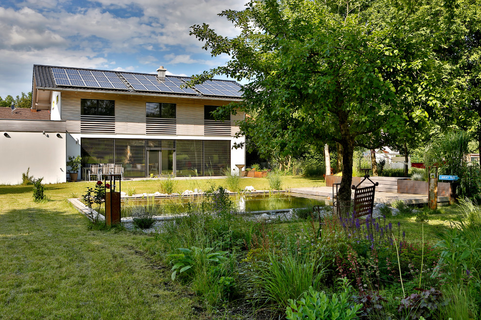 Cette image montre un grand jardin arrière design l'été avec un bassin, une exposition partiellement ombragée et une terrasse en bois.