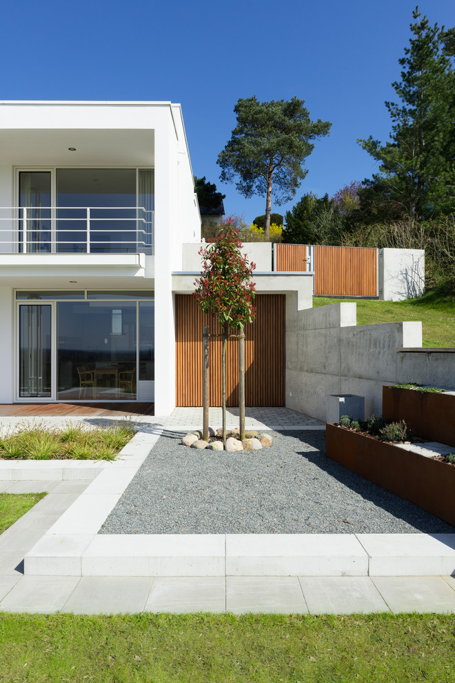Idee per un giardino formale minimal esposto in pieno sole davanti casa in primavera con un muro di contenimento e pavimentazioni in cemento