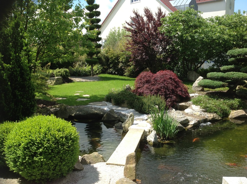 Diseño de jardín asiático de tamaño medio en verano en patio trasero con fuente, exposición parcial al sol y adoquines de piedra natural