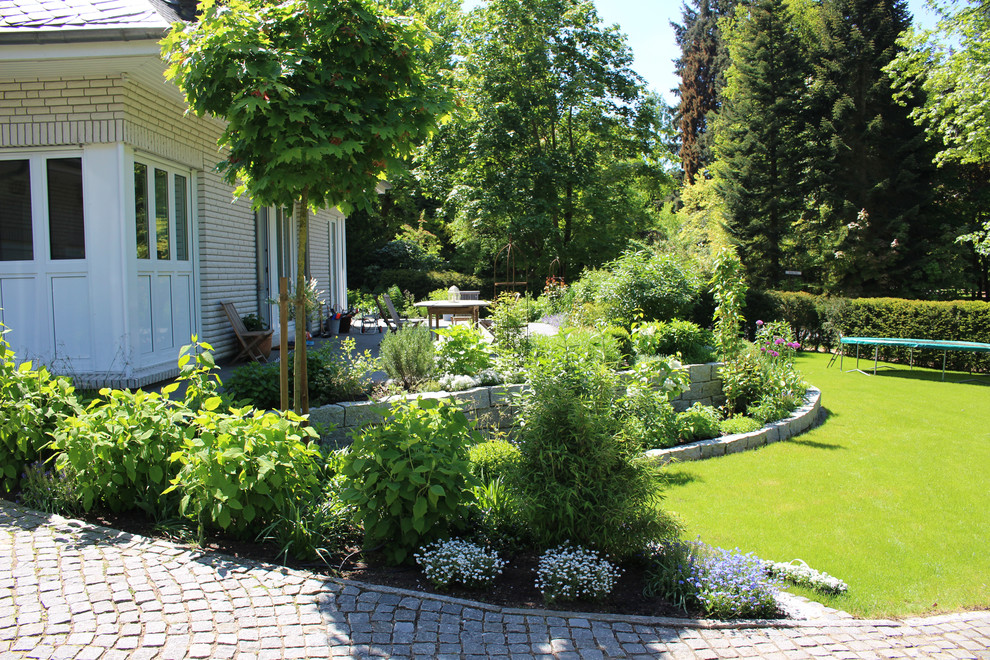 Ejemplo de jardín campestre grande en verano con muro de contención, exposición total al sol y adoquines de piedra natural