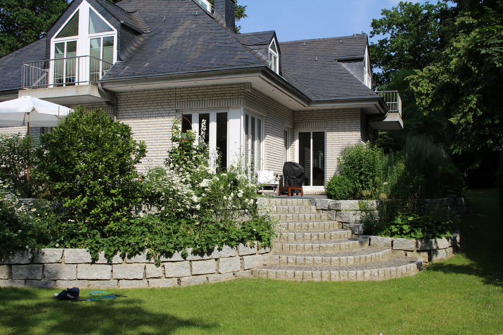 Diseño de jardín de estilo de casa de campo grande en verano con muro de contención, exposición total al sol y adoquines de piedra natural