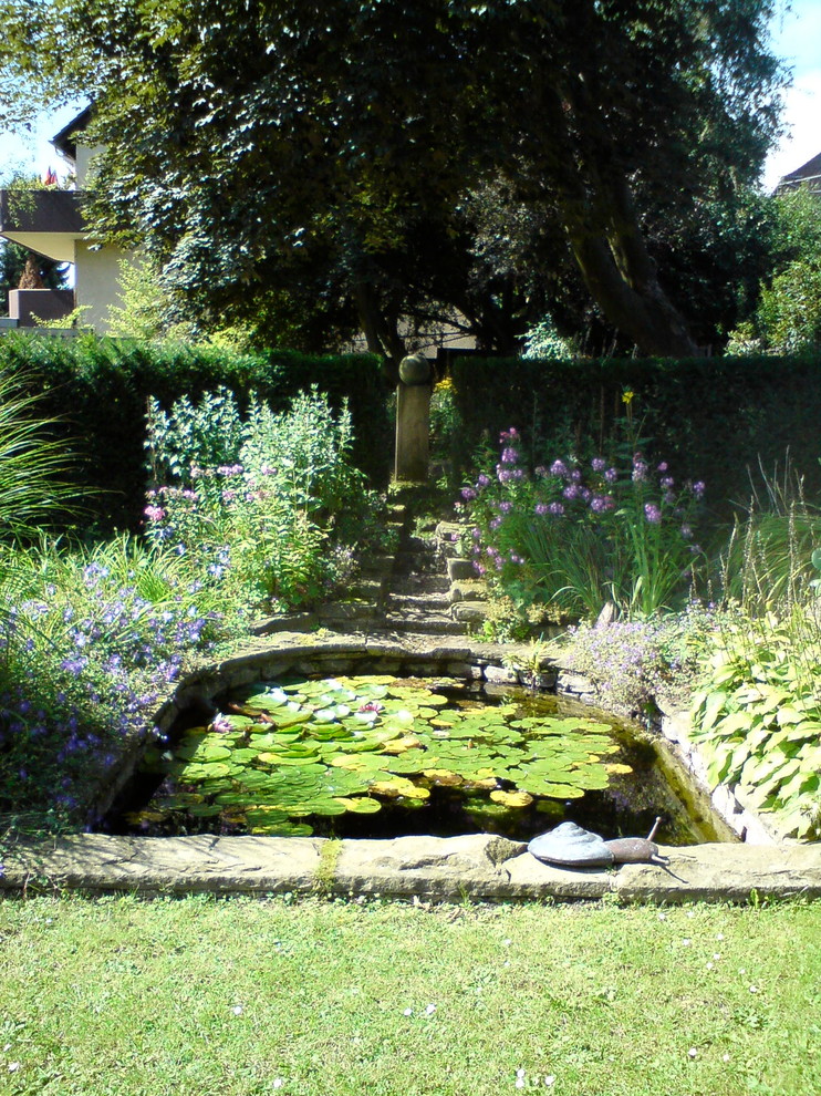 Foto på en mycket stor lantlig trädgård i delvis sol, med en damm och naturstensplattor