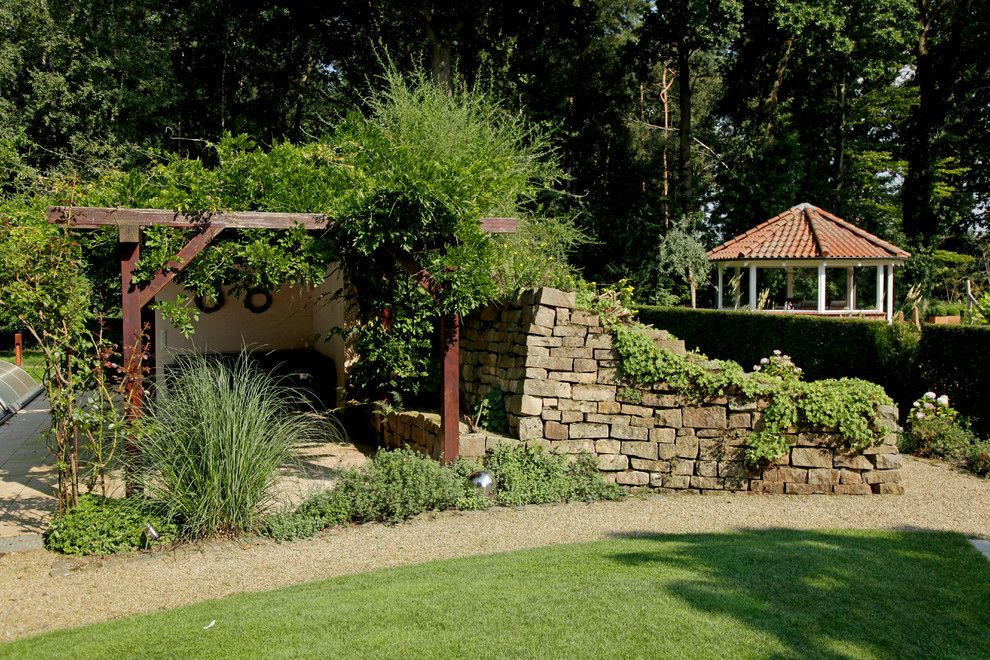 Modelo de jardín campestre en verano en patio trasero con muro de contención, adoquines de piedra natural y exposición parcial al sol