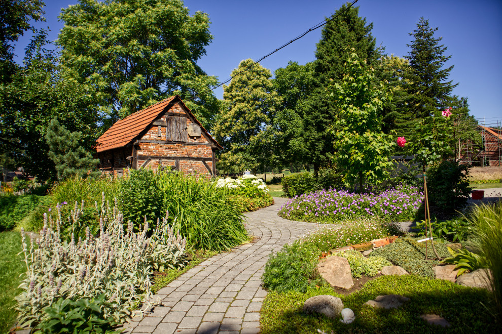 Foto på en stor lantlig bakgård i full sol på sommaren, med en trädgårdsgång och marksten i betong