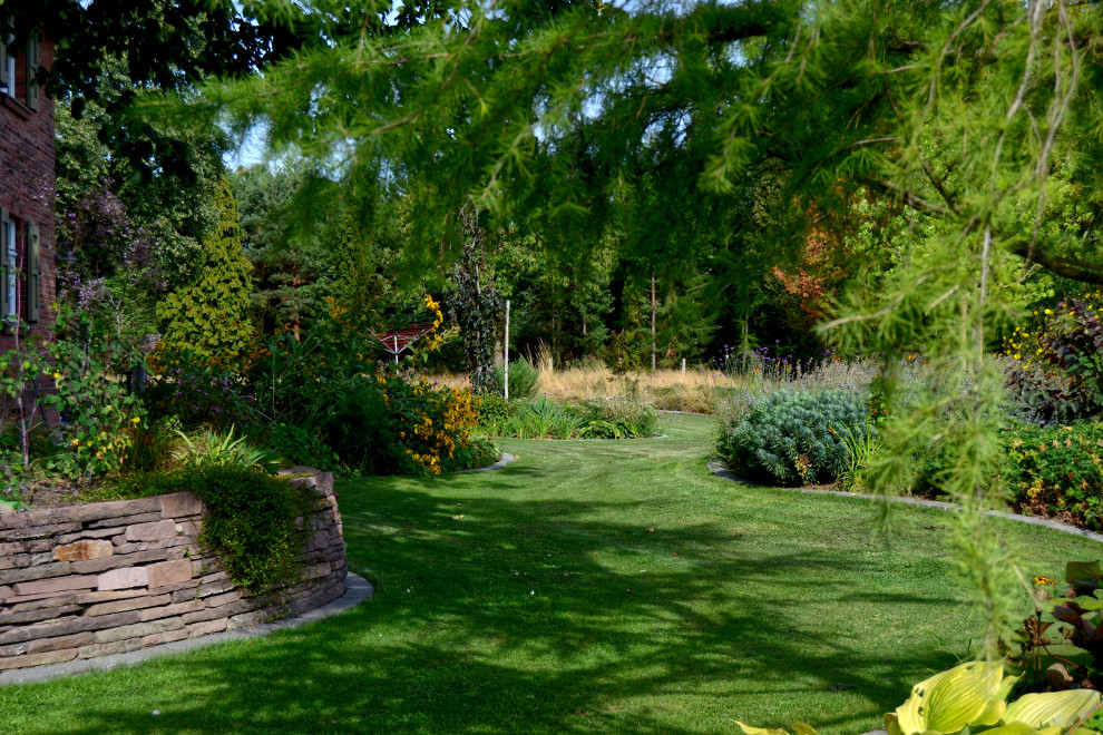 Imagen de jardín de estilo de casa de campo grande en verano en patio trasero con borde del césped, exposición parcial al sol y adoquines de hormigón