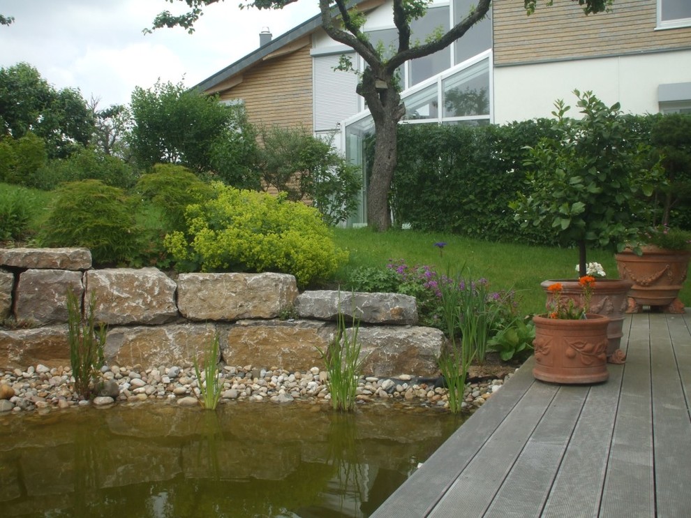 Aménagement d'un jardin classique avec un mur de soutènement et une terrasse en bois.