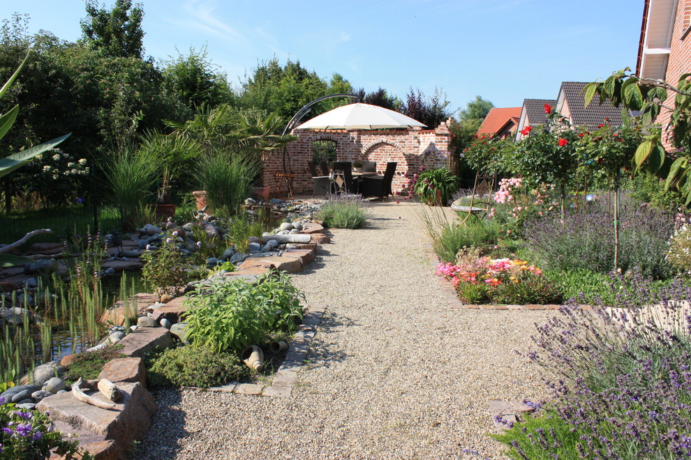 Diseño de jardín de secano mediterráneo pequeño en verano en patio trasero con muro de contención, exposición total al sol y gravilla