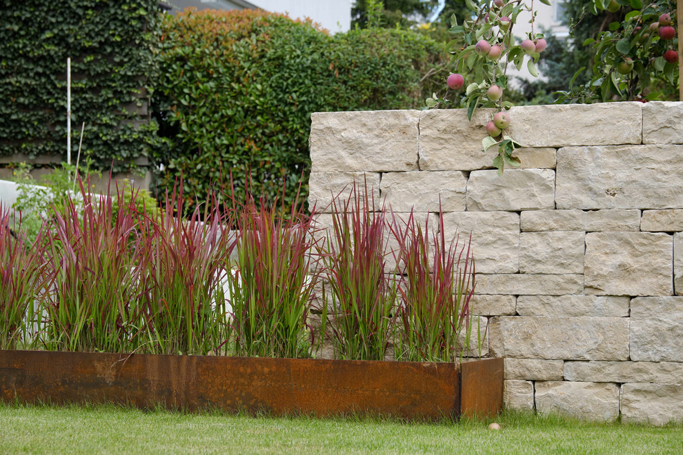 Ejemplo de jardín de secano contemporáneo grande en verano en patio trasero con muro de contención, exposición parcial al sol y adoquines de piedra natural
