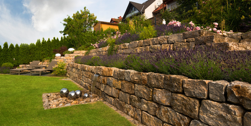 Modelo de jardín tradicional grande en verano en ladera con fuente, exposición total al sol y adoquines de piedra natural