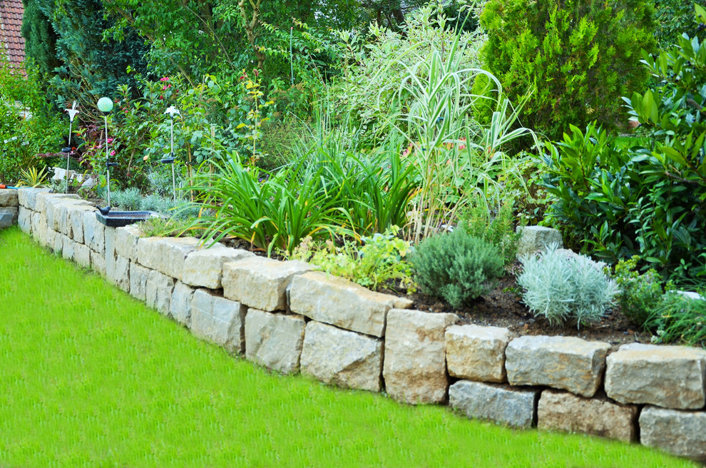 Inspiration pour un grand jardin avant traditionnel avec un mur de soutènement, une exposition ensoleillée et des pavés en pierre naturelle.
