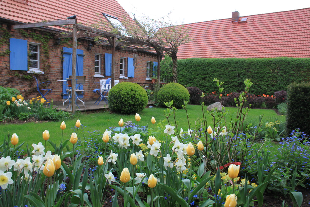 Mittelgroßer Landhaus Garten im Frühling, hinter dem Haus mit direkter Sonneneinstrahlung und Pergola in Berlin