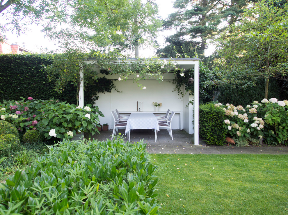 Imagen de jardín clásico de tamaño medio en verano en patio lateral con jardín francés, exposición parcial al sol y adoquines de hormigón