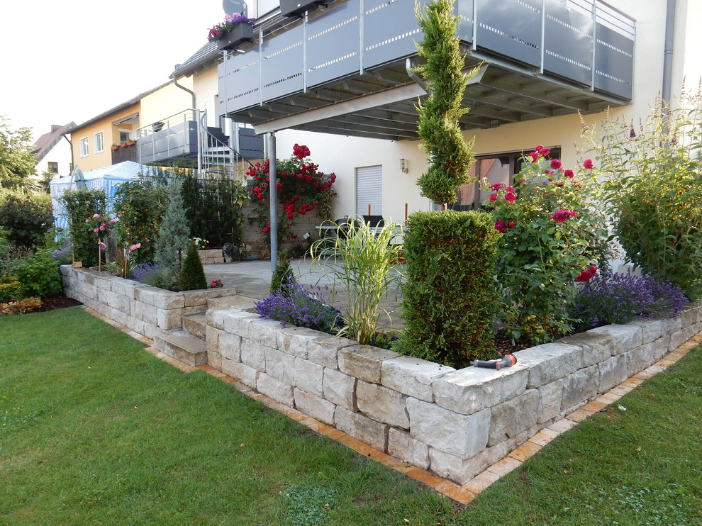 Modelo de jardín campestre en patio trasero con muro de contención y adoquines de piedra natural