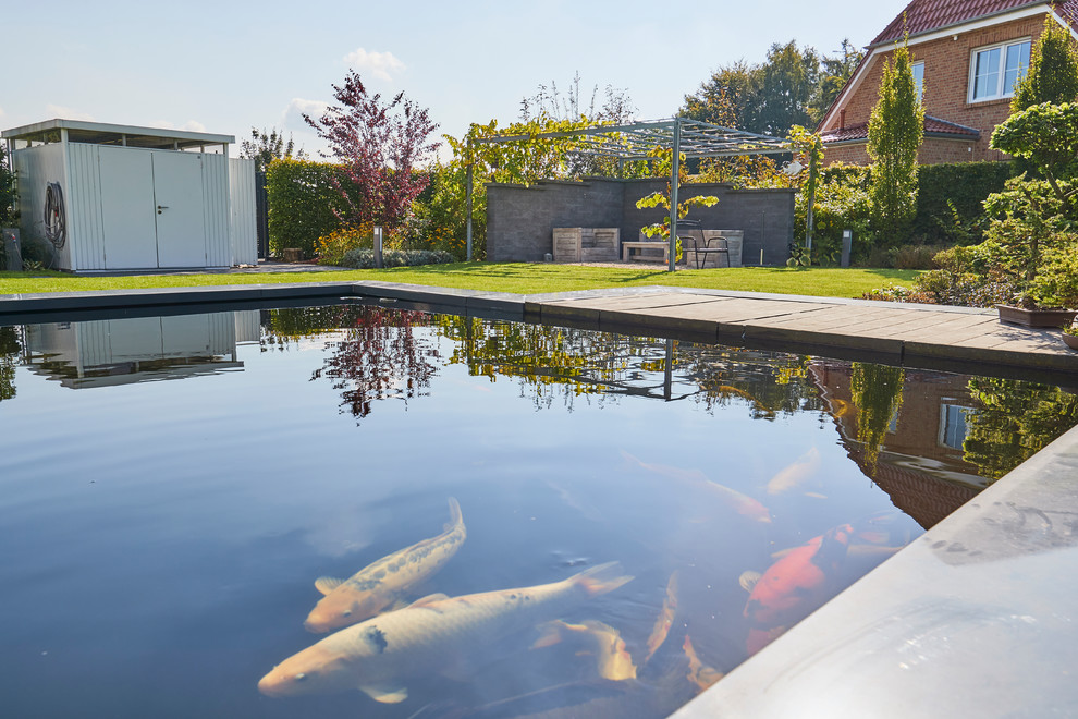 Cette image montre un très grand jardin arrière design avec un bassin, une exposition ensoleillée et des pavés en béton.