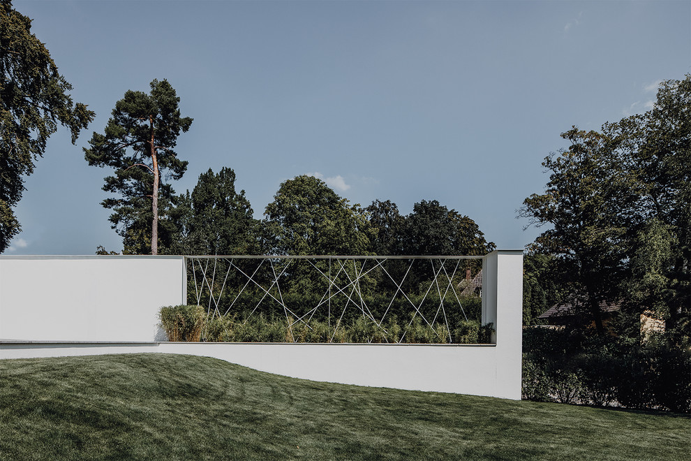 Foto di un grande giardino minimalista esposto in pieno sole davanti casa in estate con un muro di contenimento e pavimentazioni in pietra naturale