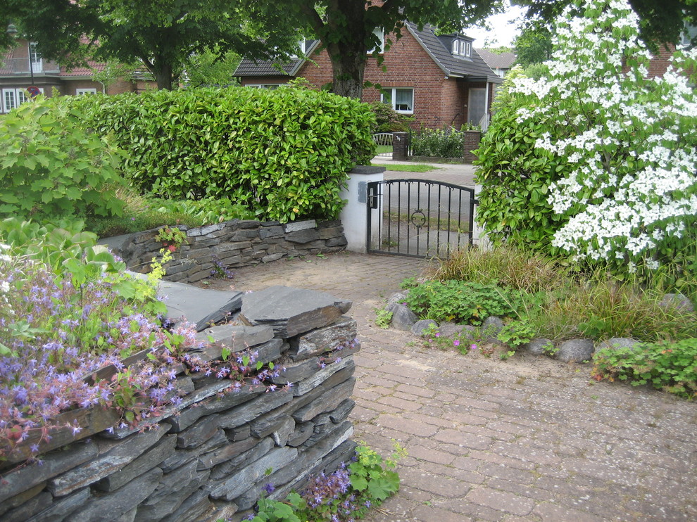 Immagine di un piccolo giardino rustico esposto in pieno sole davanti casa in estate con un muro di contenimento e pavimentazioni in pietra naturale