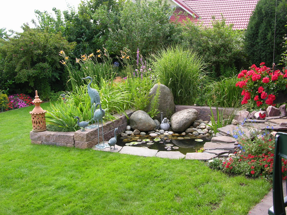 Modelo de jardín mediterráneo grande en verano en patio trasero con adoquines de piedra natural, jardín francés, estanque y exposición total al sol