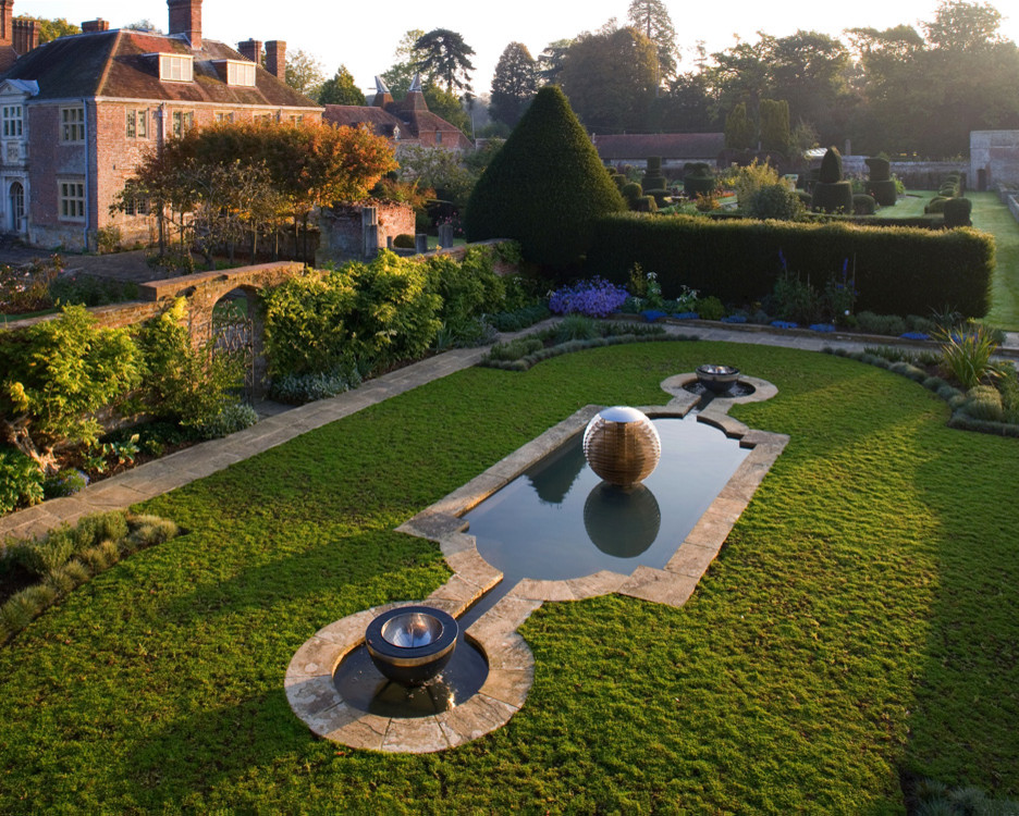 Immagine di un grande giardino formale vittoriano esposto in pieno sole dietro casa con fontane e pavimentazioni in pietra naturale