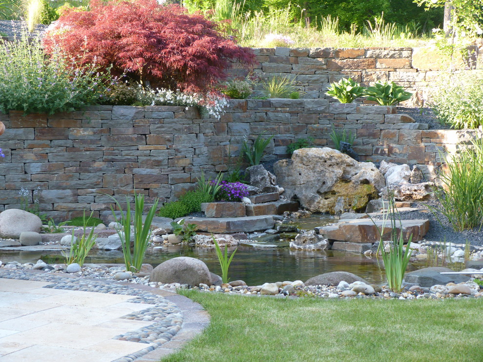 На фото: большой солнечный, весенний участок и сад на склоне в стиле кантри с подпорной стенкой, хорошей освещенностью и покрытием из каменной брусчатки