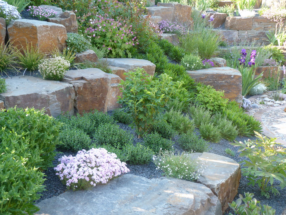 Imagen de jardín campestre grande en primavera en ladera con muro de contención, exposición total al sol y adoquines de piedra natural