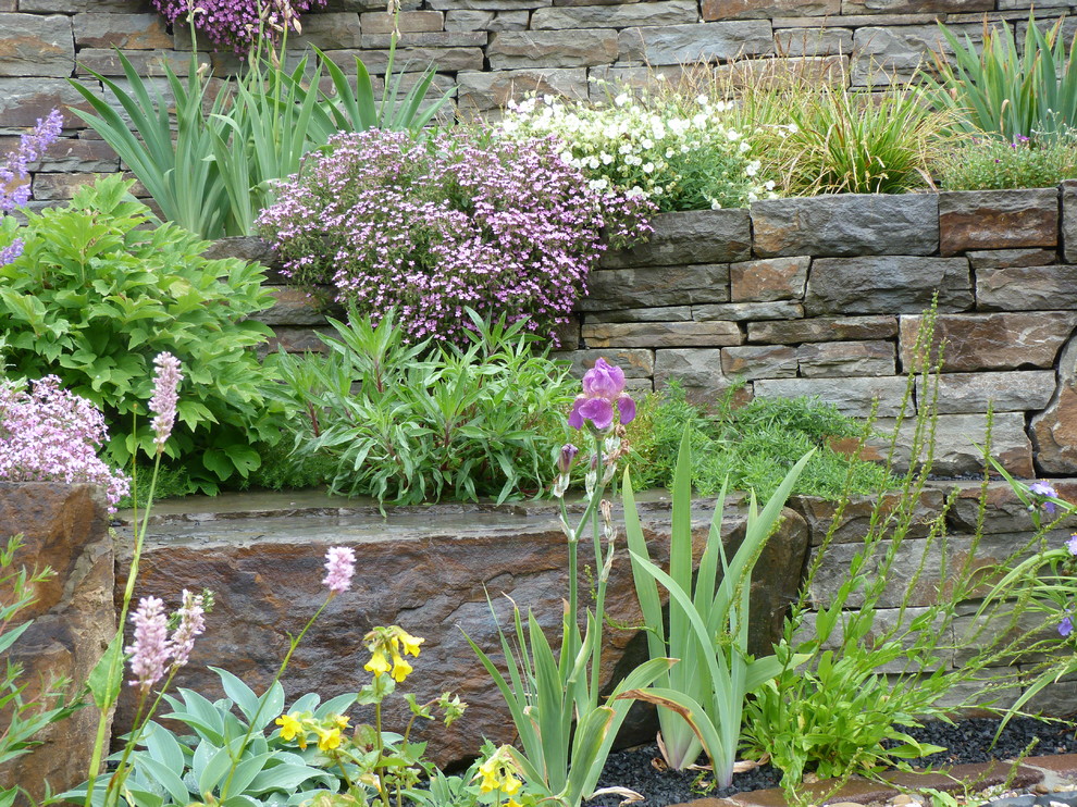 Imagen de jardín campestre grande en primavera en ladera con muro de contención, exposición total al sol y adoquines de piedra natural