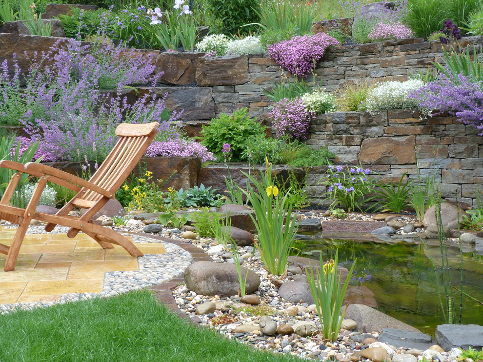 Immagine di un grande giardino country esposto in pieno sole in primavera con un muro di contenimento, un pendio, una collina o una riva e pavimentazioni in pietra naturale
