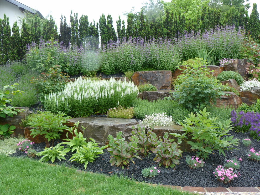 Réalisation d'un grand jardin champêtre l'été avec un mur de soutènement, une exposition ensoleillée, une pente, une colline ou un talus et des pavés en pierre naturelle.