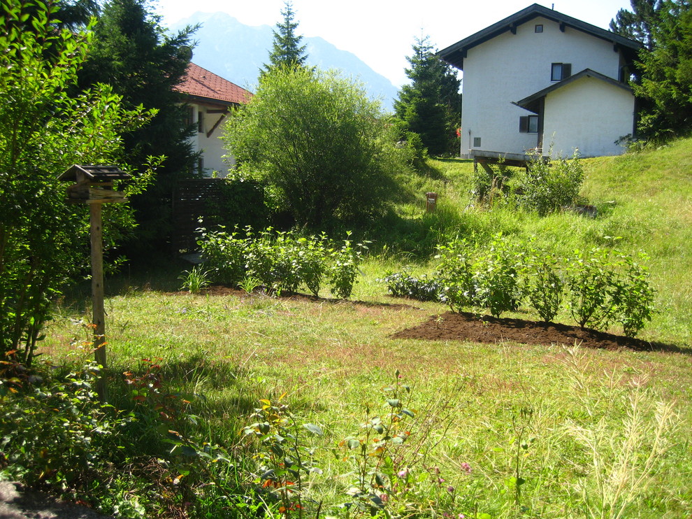Inredning av en lantlig mellanstor formell trädgård i full sol i slänt på sommaren, med utekrukor och marksten i betong