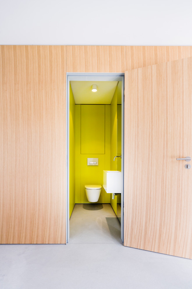 Kleine Moderne Gästetoilette mit flächenbündigen Schrankfronten, hellen Holzschränken, grüner Wandfarbe, Betonboden und grauem Boden in Stuttgart