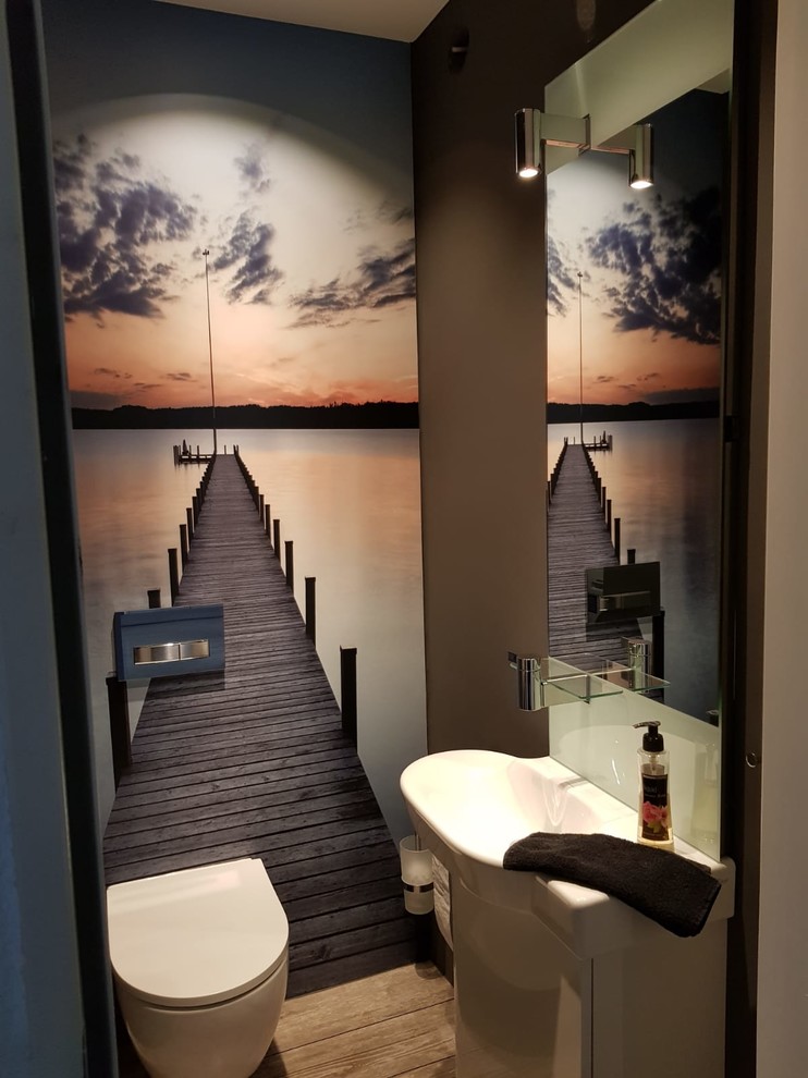 ハンブルクにある小さなコンテンポラリースタイルのおしゃれなトイレ・洗面所 (フラットパネル扉のキャビネット、白いキャビネット、分離型トイレ、茶色い壁、塗装フローリング、茶色い床) の写真