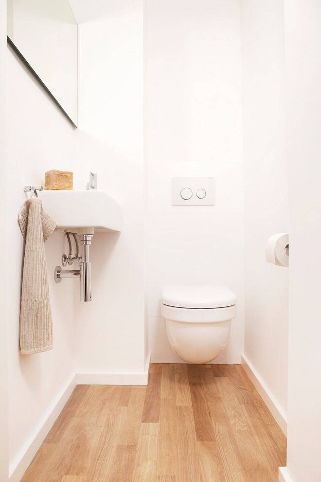 Idee per un piccolo bagno di servizio scandinavo con WC sospeso, pareti bianche, parquet chiaro, lavabo sospeso e pavimento marrone