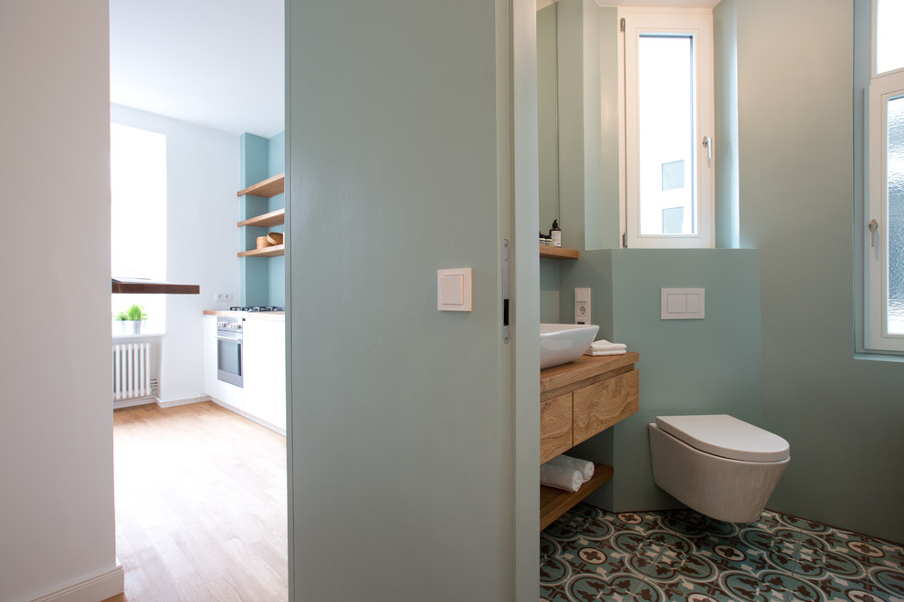 Immagine di un bagno di servizio nordico con ante lisce, ante in legno scuro, WC sospeso, pavimento in cementine, lavabo a bacinella, top in legno, pavimento multicolore e top marrone