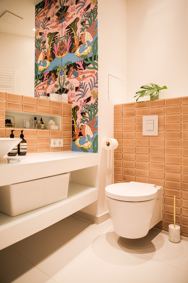 Small eclectic cloakroom in Berlin with open cabinets, a two-piece toilet, pink tiles, metro tiles, a trough sink, glass worktops, white walls, ceramic flooring and beige floors.