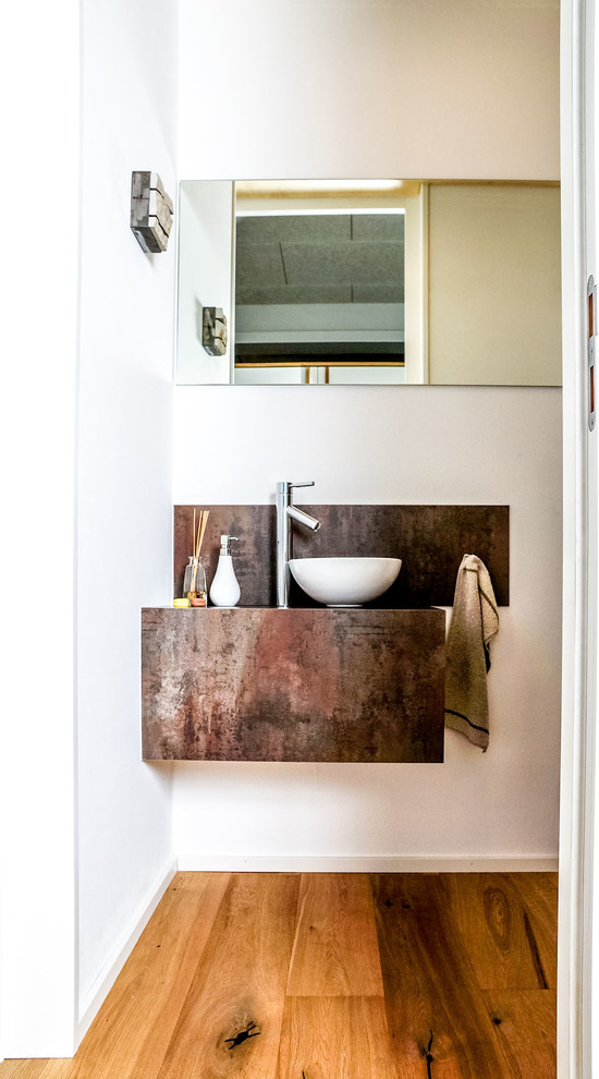 Kleine Industrial Gästetoilette mit weißer Wandfarbe, braunem Holzboden, Aufsatzwaschbecken und orangem Boden in Sonstige