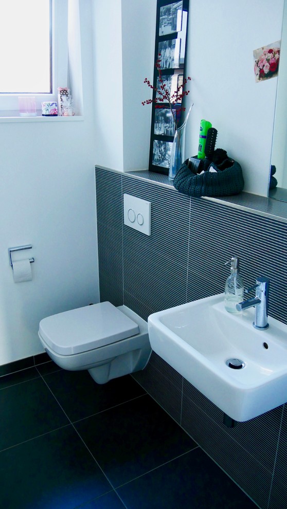 Inspiration för små moderna toaletter, med en toalettstol med separat cisternkåpa, svart kakel, vita väggar, ett väggmonterat handfat, svart golv, stickkakel och cementgolv