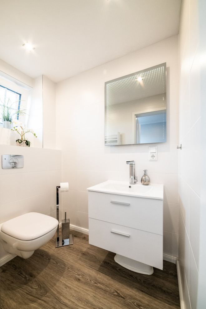 Cette photo montre un petit WC suspendu moderne avec un placard à porte plane, des portes de placard blanches, un carrelage blanc, des carreaux de céramique, un mur blanc, un sol en vinyl, un lavabo posé, un plan de toilette en bois, un sol gris et un plan de toilette blanc.