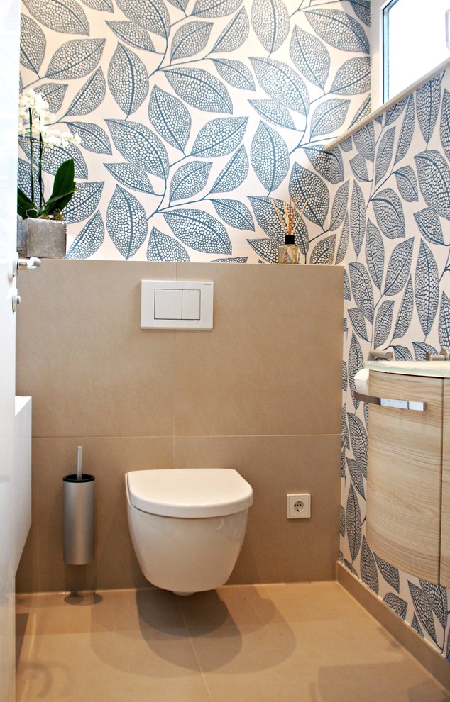 На фото: туалет среднего размера в современном стиле с бежевой плиткой, светлыми деревянными фасадами, инсталляцией, накладной раковиной, стеклянной столешницей и разноцветными стенами