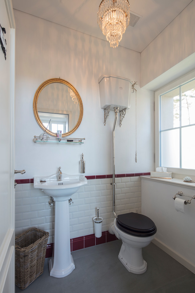 Bild på ett litet vintage toalett, med en toalettstol med separat cisternkåpa, röd kakel, vit kakel, tunnelbanekakel, vita väggar, cementgolv, ett piedestal handfat, bänkskiva i akrylsten och grått golv
