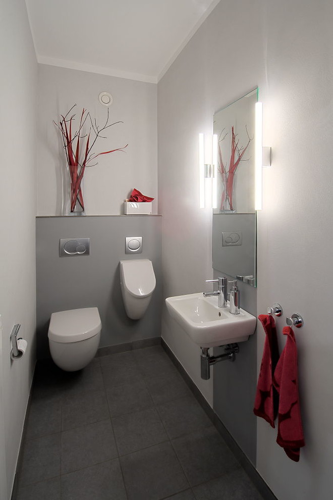 Cette image montre un petit WC et toilettes design avec un urinoir, un carrelage gris, un mur gris et un lavabo suspendu.