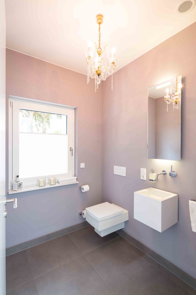 Imagen de aseo clásico pequeño con paredes púrpuras, suelo gris, sanitario de dos piezas y lavabo suspendido