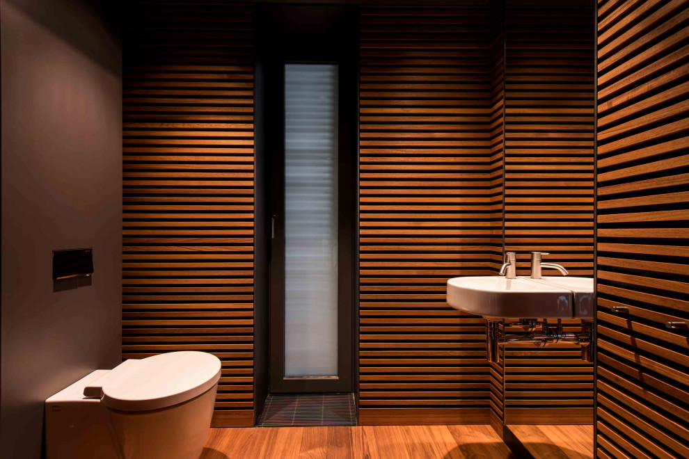 Foto di un bagno di servizio contemporaneo di medie dimensioni con WC sospeso, pareti marroni, lavabo sospeso, pavimento marrone e pareti in legno