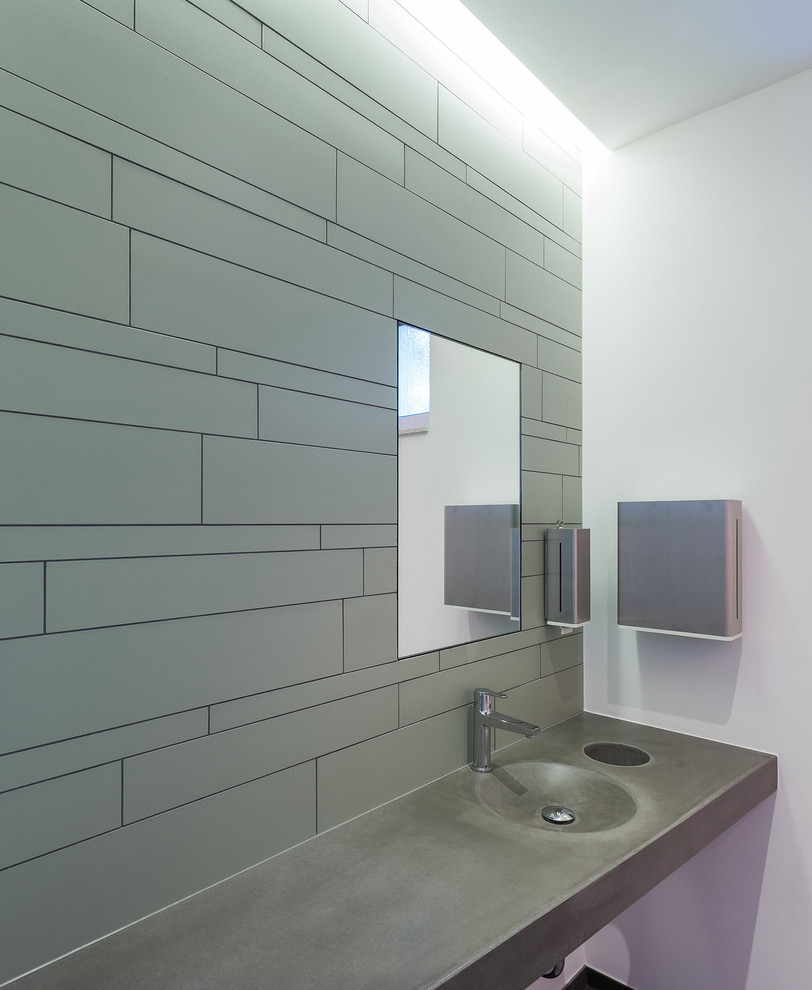 Exempel på ett mellanstort industriellt toalett, med en vägghängd toalettstol, grön kakel, stenkakel, vita väggar, klinkergolv i keramik, bänkskiva i betong och ett integrerad handfat