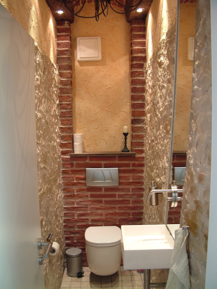 Design ideas for a small mediterranean cloakroom in Munich with a wall mounted toilet, beige tiles, limestone tiles, beige walls, marble flooring, a wall-mounted sink, solid surface worktops, beige floors, white worktops, feature lighting, a floating vanity unit, a vaulted ceiling and wainscoting.