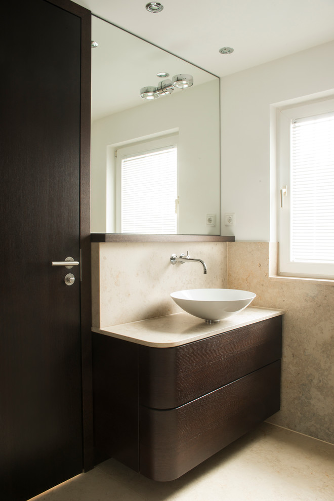 Photo of a medium sized contemporary cloakroom in Dusseldorf with flat-panel cabinets, dark wood cabinets, beige tiles, white walls, marble flooring, a vessel sink and stone slabs.