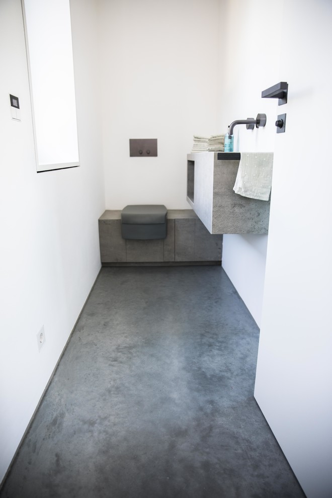Idées déco pour un petit WC et toilettes moderne avec sol en béton ciré, un placard sans porte, des portes de placard grises, WC séparés, un mur blanc, un lavabo suspendu, un plan de toilette en béton et un sol gris.
