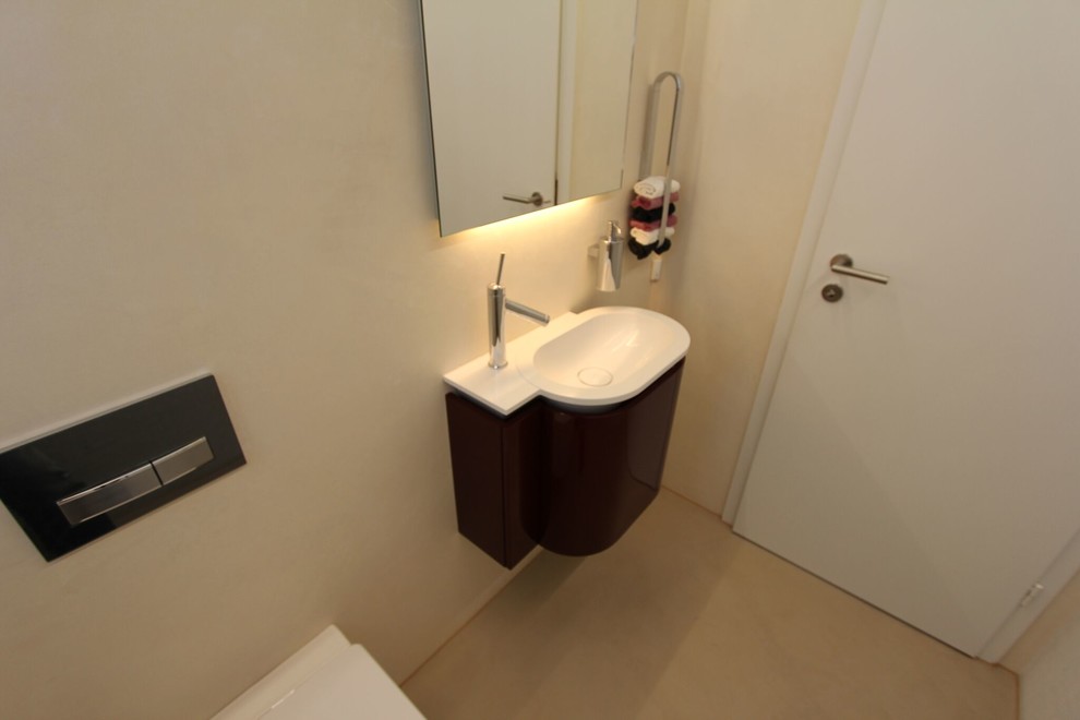 Réalisation d'un WC suspendu design de taille moyenne avec un placard à porte plane, des portes de placard grises, un carrelage beige, un mur beige, sol en béton ciré, un lavabo intégré, un plan de toilette en surface solide et un sol beige.